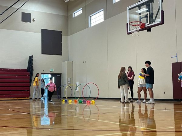 A Group of PEOPEL PE students and helpers set up an obstacle course during class. The “Amazing Race” unit had started in PEOPEL PE where the students and helpers got to compete in a variety of different activities and games. “We try our best to make [inclusion] a school-wide event, but it's just so much more different when you actually engage with the students hands-on and actually get to know them as people.” Sophomore Bree Christensen said. Photo Taken by Ada McNulty.